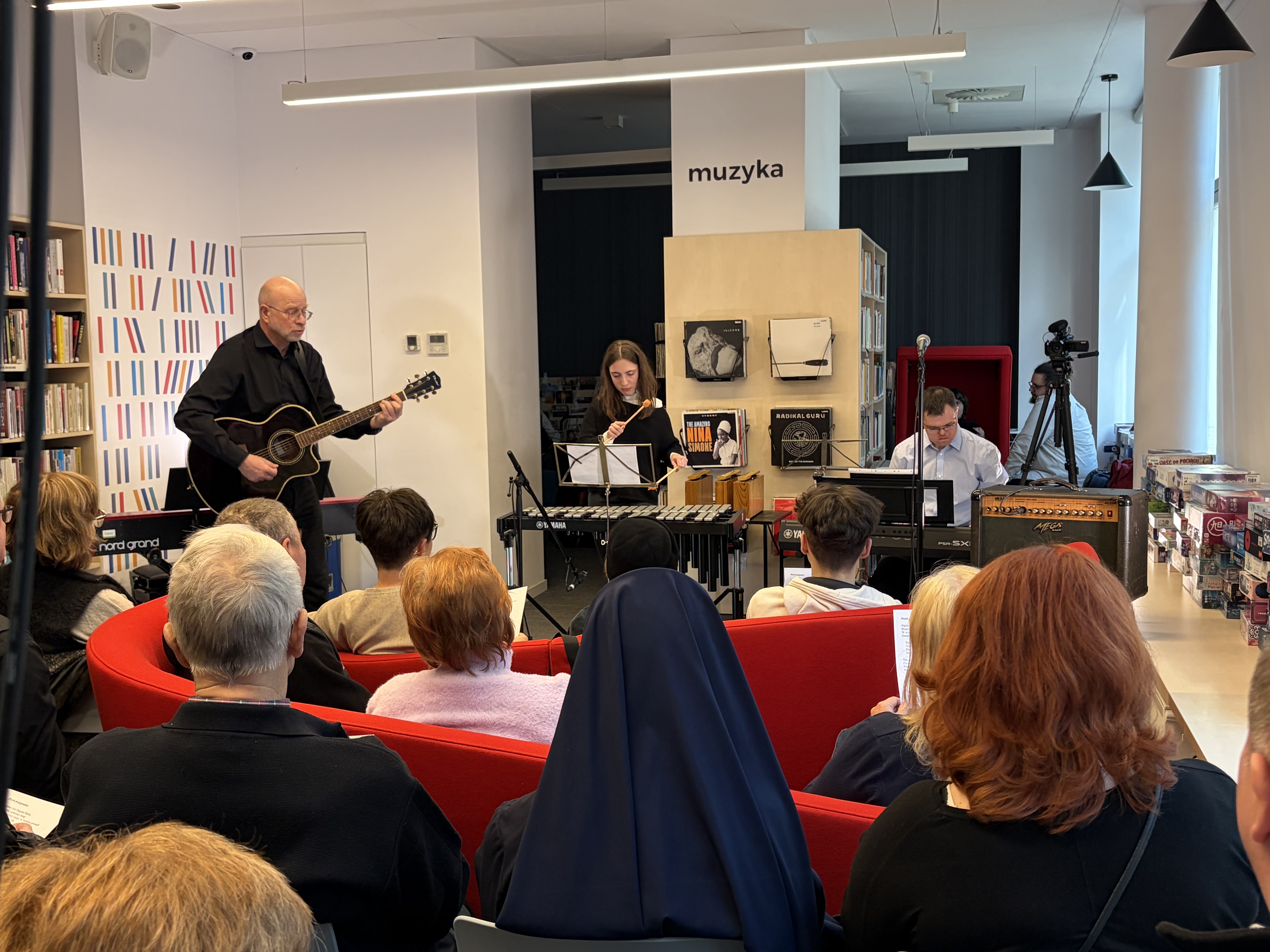 Koncert zespołu ECEKON. Mężczyzna gra na gitarze, obok kobieta gra na cymbałkach, a po prawej stronie mężczyzna gra na klawiszach.